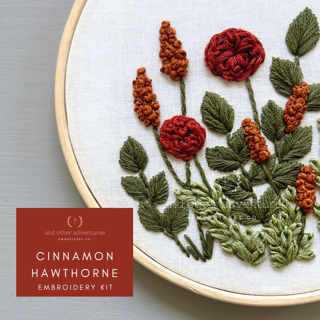 Embroidery hoop with embroidered flowers and leaves, featuring 'Cinnamon Hawthorne' embroidery kit branding.