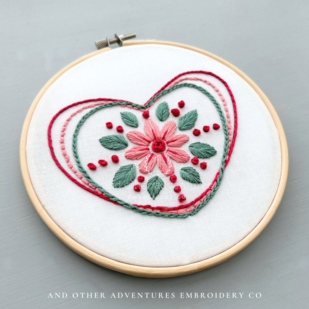 Embroidery hoop with floral design on a white fabric background created by And Other Adventures Embroidery Co