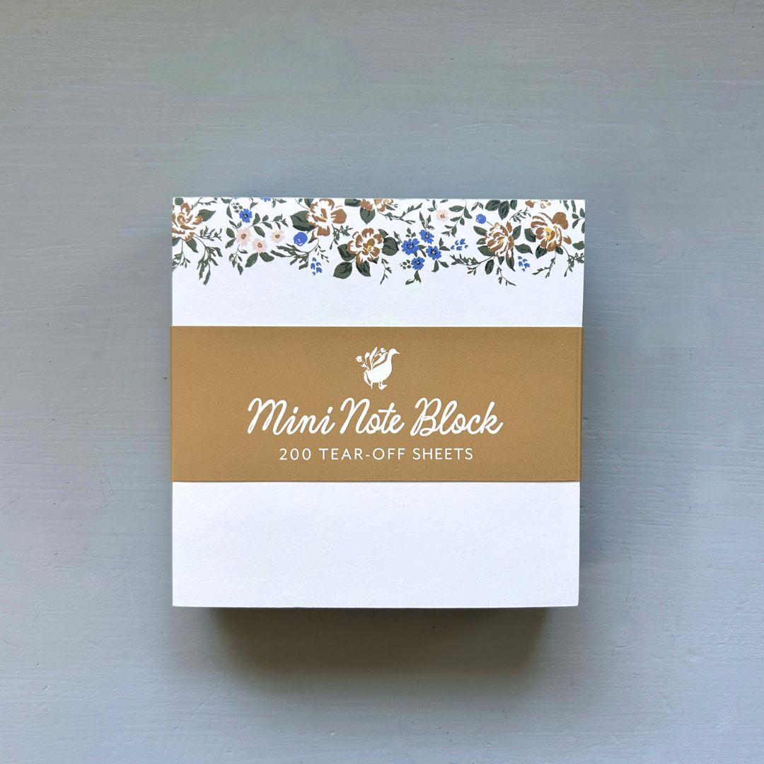 Mini note block with floral design on top and text on a plain background