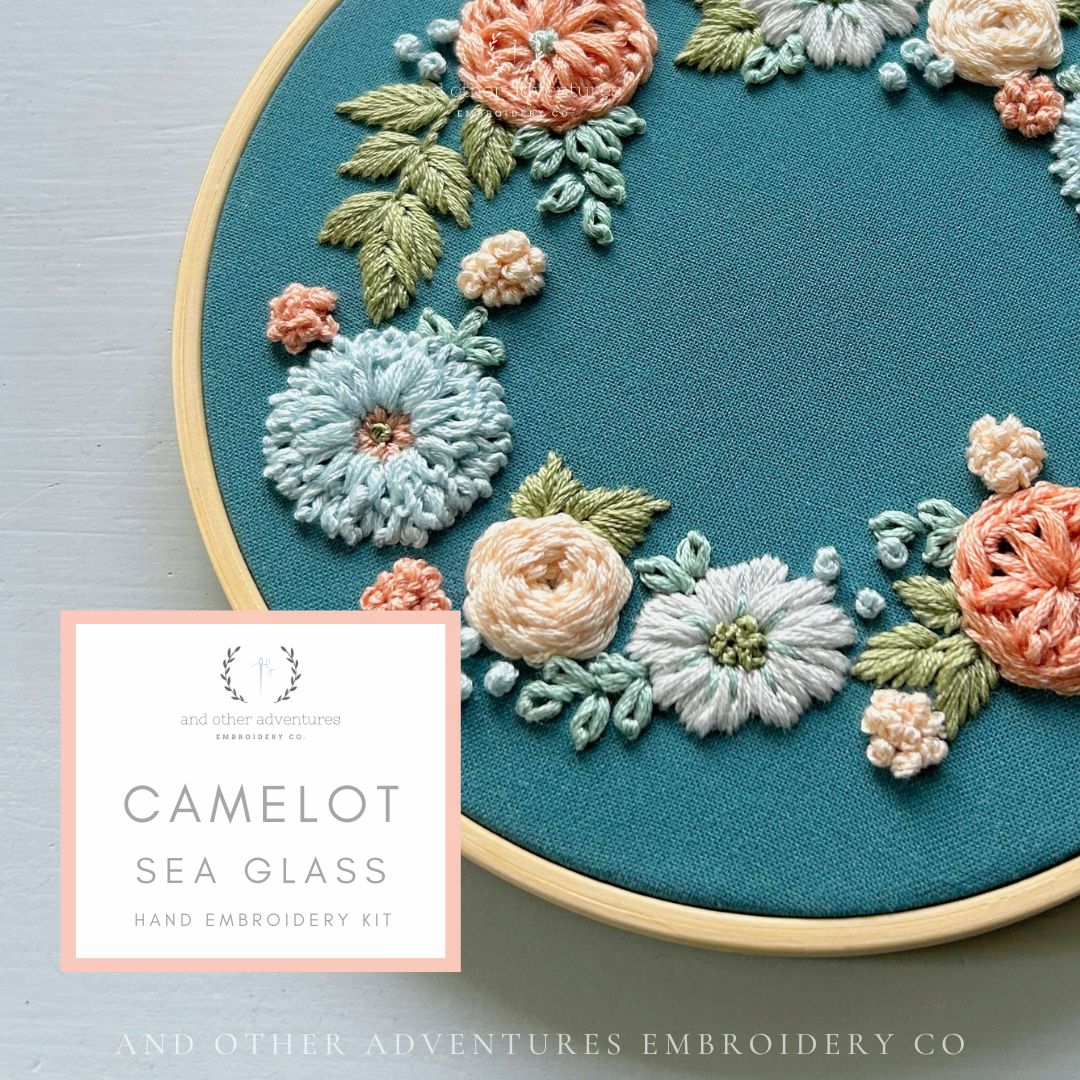 Embroidery hoop with floral embroidery design on teal fabric, featuring 'Camelot Sea Glass' kit by And Other Adventures Embroidery Co.
