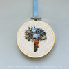 Embroidery hoop with navy, olive green and mustard floral design on a light gray background, featuring the brand &#39;And Other Adventures Embroidery Co&#39;.