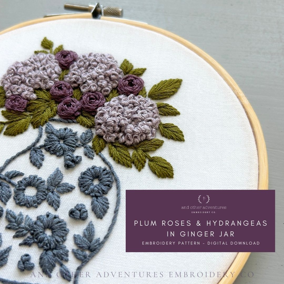 Embroidery hoop with plum roses, hydrangeas, and ginger jar design on white fabric.