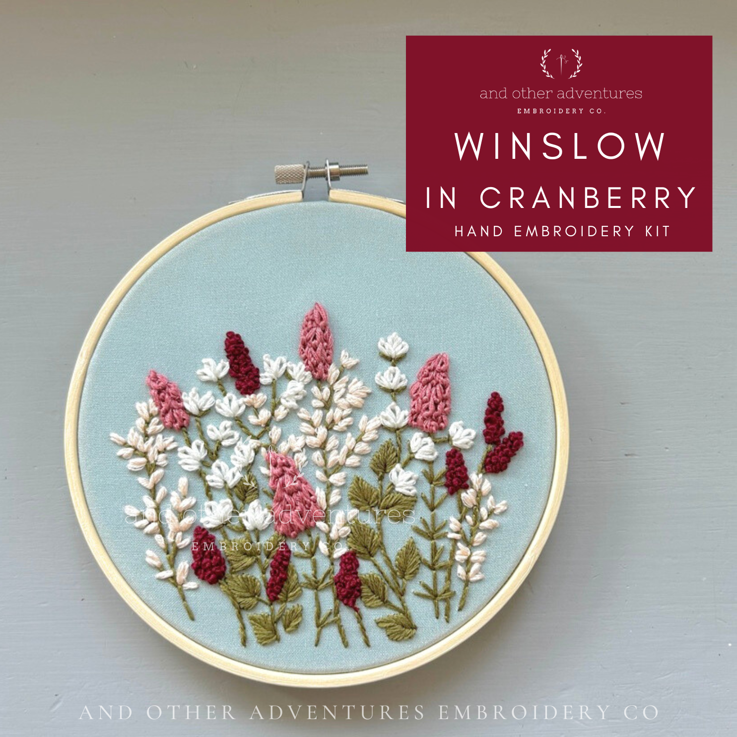 Embroidery hoop with floral embroidery on a pale sage background, featuring 'Winslow in Cranberry' hand embroidery kit by And Other Adventures Embroidery Co.
