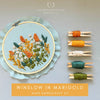 Hand embroidery kit with completed design, threads, and tools on a light gray background.