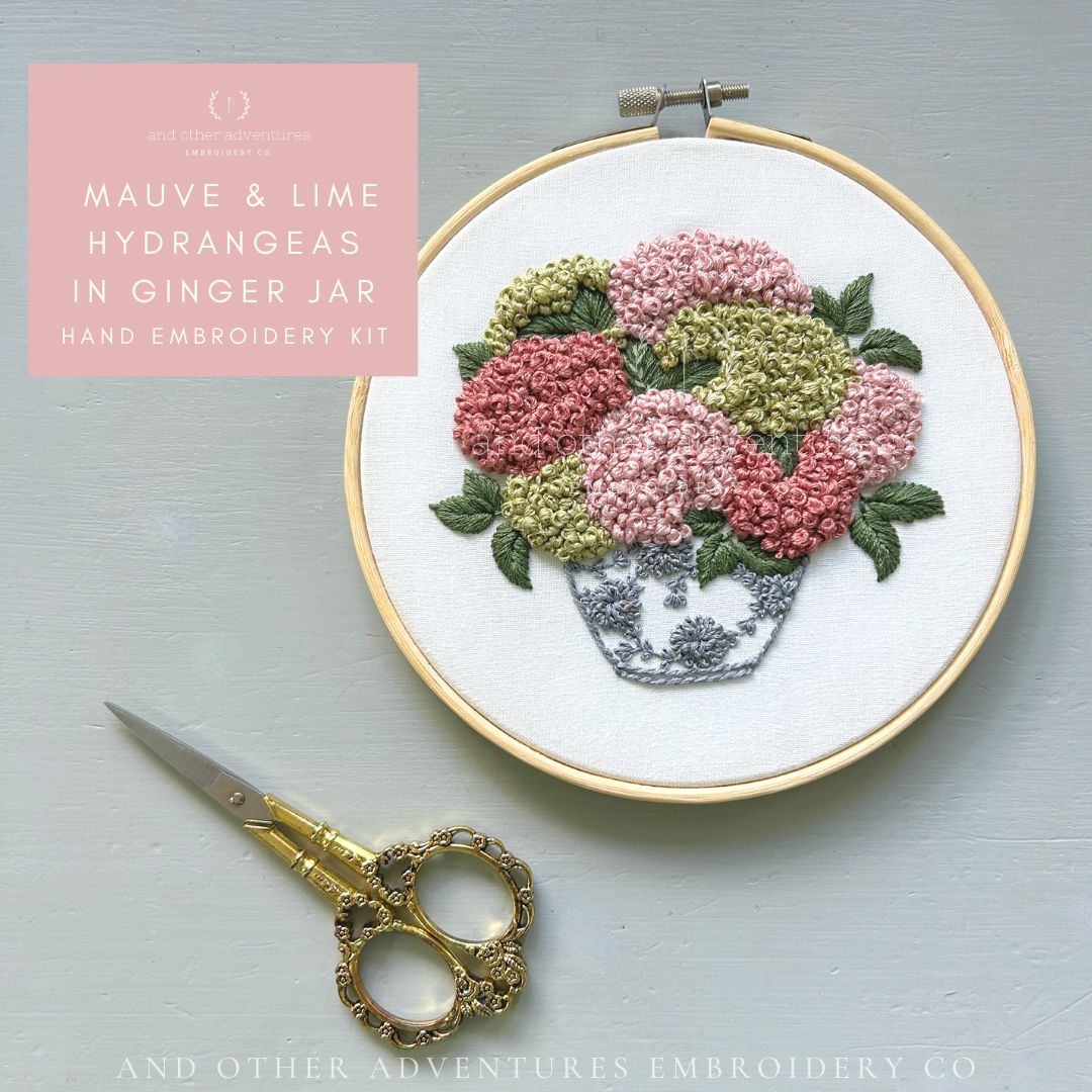 Embroidery hoop with floral design and scissors on a gray background, featuring &#39;And Other Adventures Embroidery Co&#39; branding.